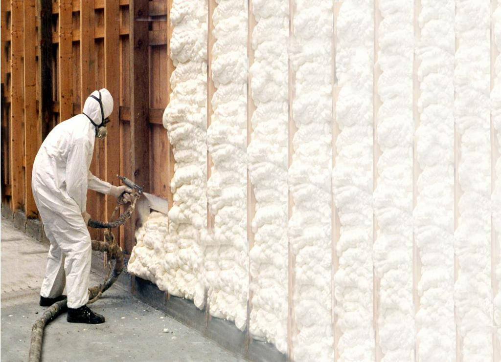 Contractor in PPE applying spray foam insulation to wall studs
