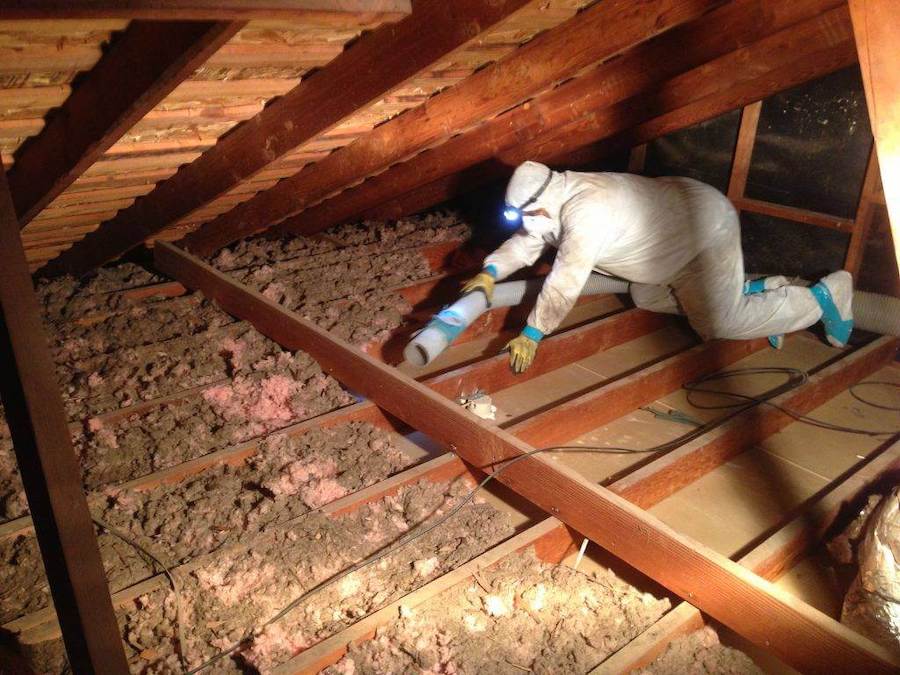 Contractor with headlamp crawling through attic removing insulation
