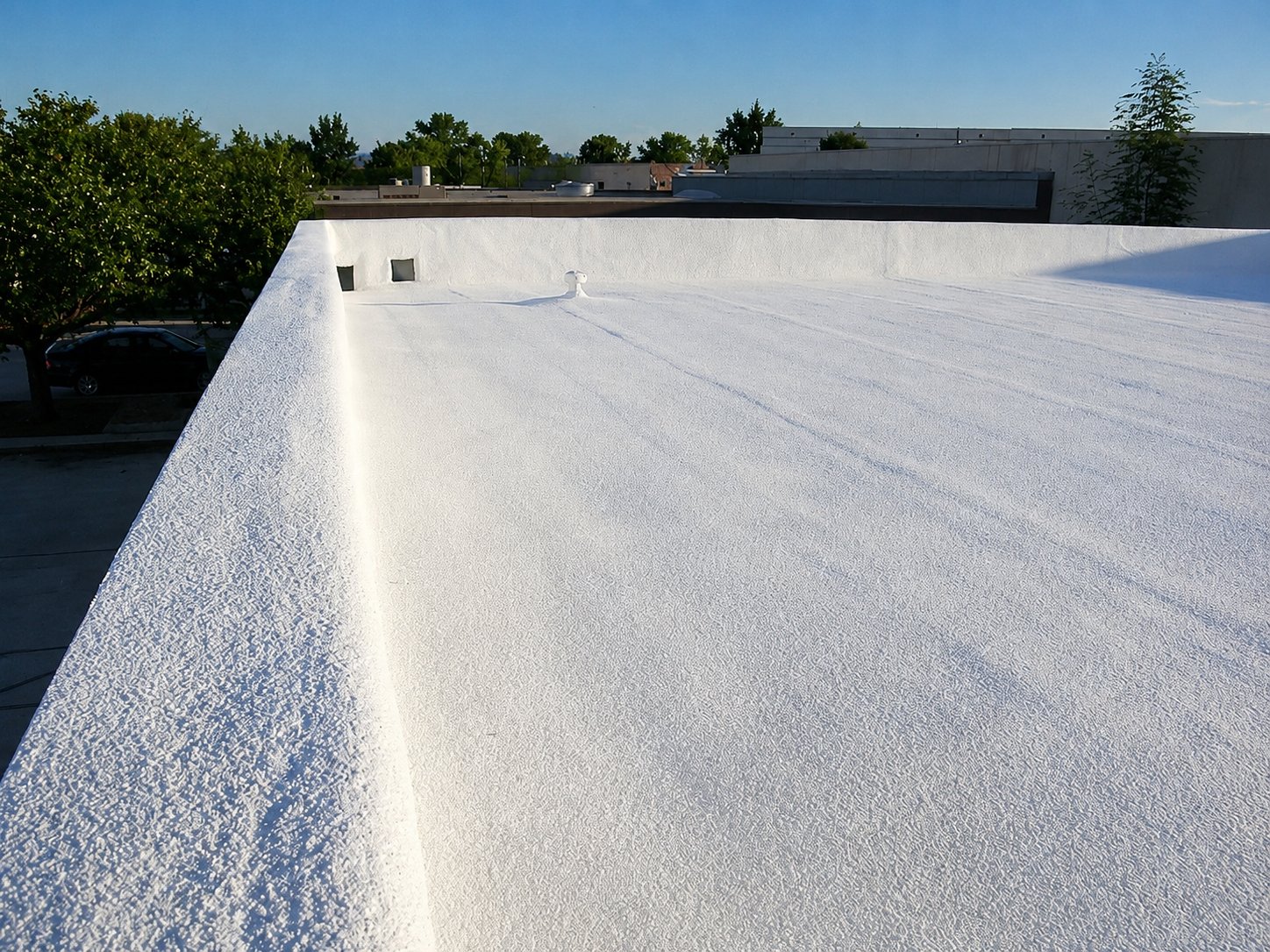 Finished white spray foam roof edge on commercial building with parking lot view