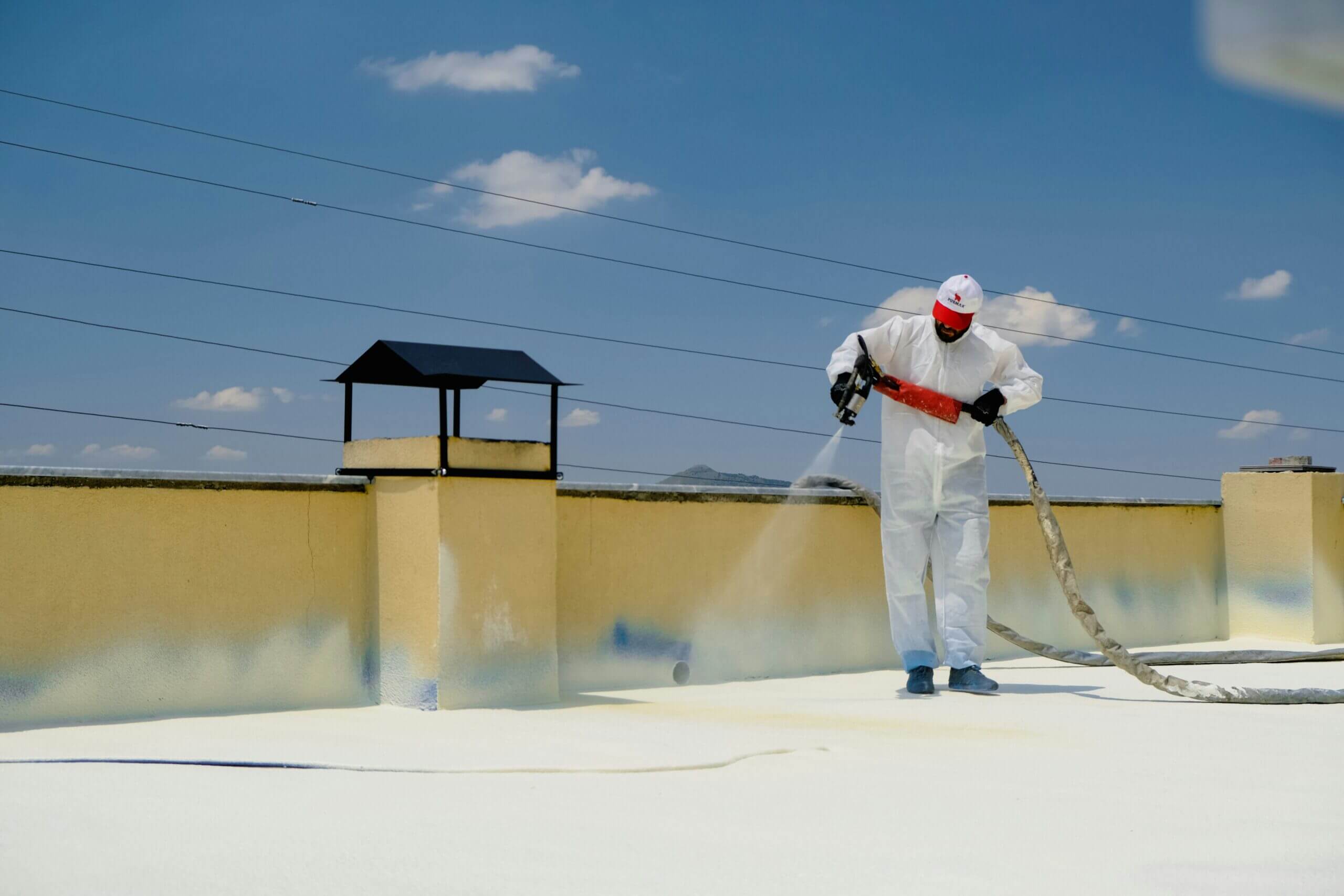 Technician spray-applying foam roof coating on commercial building